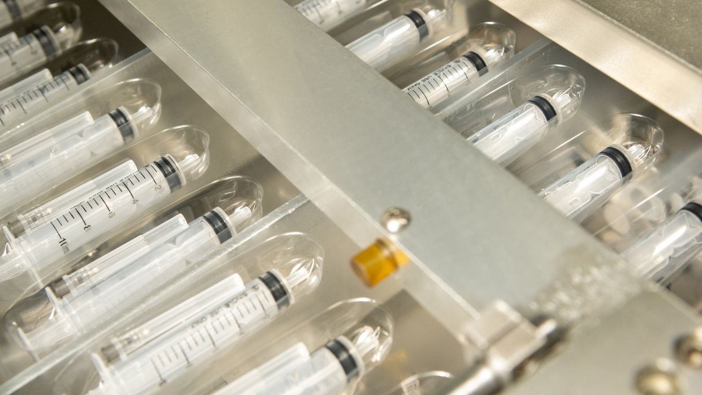 Sterile syringes on a conveyor belt tracked by healthcare supply chain software.